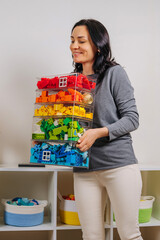 Young woman is holding storage boxes toys. Mom sorted by colors children's toys in transparent...