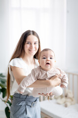 a happy, smiling little newborn baby girl in her mother's arms in close-up focus at home in the sleeping nursery by the bed. Mother's love