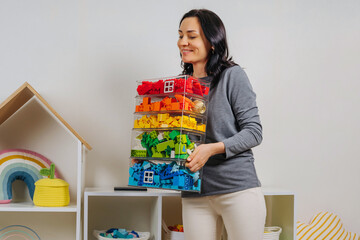 Young woman is holding storage boxes toys. Mom sorted by colors children's toys in transparent...