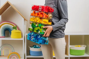 Fotobehang Young woman is holding storage boxes toys. Mom sorted by colors children's toys in transparent plastic boxes. Mother tidy up the children's room. Organization and Storage Ideas in playroom. © igishevamaria
