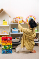 Mom sorted by colors and puts children's toys in transparent boxes and storage baskets. Mother tidy up the childrens room. Organization and Storage Ideas in playroom.