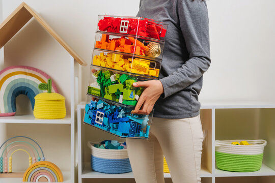 Young woman is holding storage boxes toys. Mom sorted by colors children's toys in transparent plastic boxes. Mother tidy up the children's room. Organization and Storage Ideas in playroom.