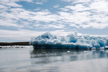 View of a blue iceberg broken off from the glacier tongue of Fjallsjökull in the glacier lagoon Fjallsárlón in Iceland on a cloudy day. With a view of Öræfajökull in the background.