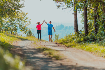 Couple enjoying in a healthy lifestyle while jogging on a country road through the beautiful sunny forest, exercise and fitness concept