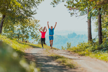 Couple enjoying in a healthy lifestyle while jogging on a country road through the beautiful sunny forest, exercise and fitness concept