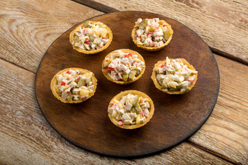 Salad in tartlets with shrimps and pineapple on a round wooden board.