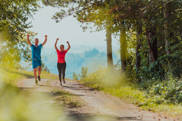 Fototapeta premium Couple enjoying in a healthy lifestyle while jogging on a country road through the beautiful sunny forest, exercise and fitness concept