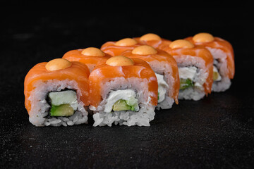 salmon sushi roll with spicy sauce on top on black background