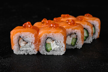 salmon sushi roll with red caviar on top on black background