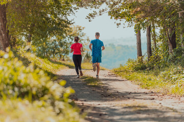 Fototapeta premium Couple enjoying in a healthy lifestyle while jogging on a country road through the beautiful sunny forest, exercise and fitness concept