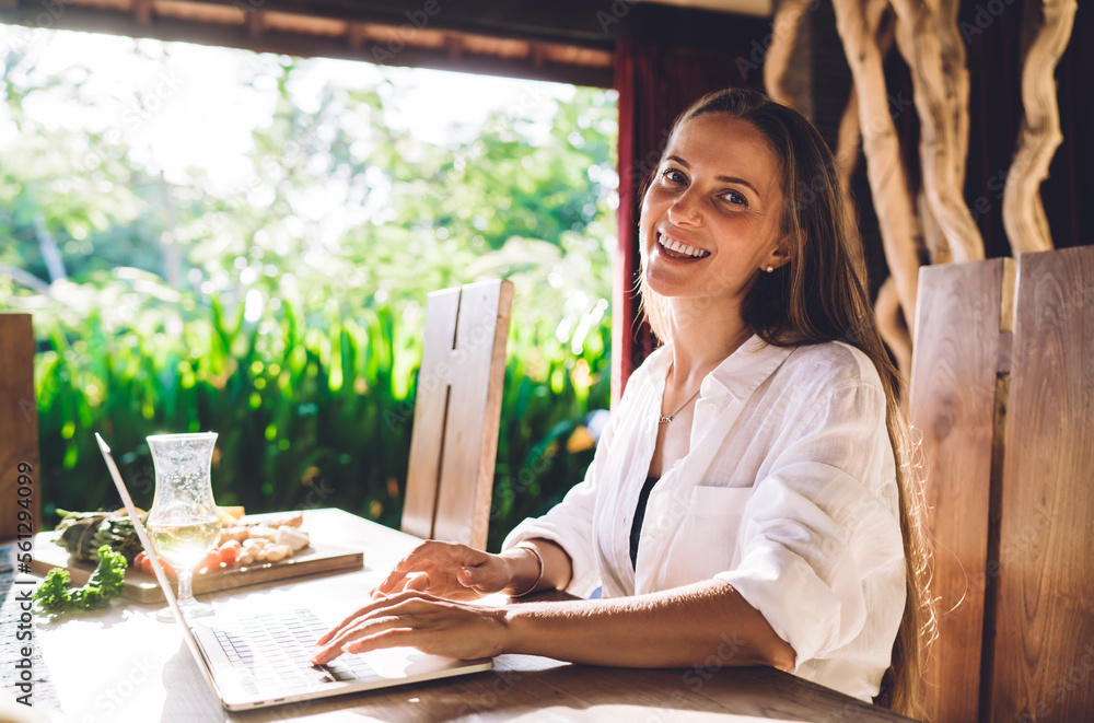 Poster portrait of cheerful female freelancer smiling at camera during time for doing distance startup proj