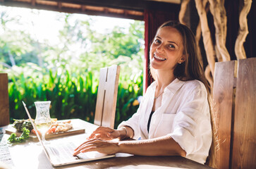 Portrait of cheerful female freelancer smiling at camera during time for doing distance startup...
