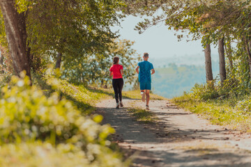 Fototapeta premium Couple enjoying in a healthy lifestyle while jogging on a country road through the beautiful sunny forest, exercise and fitness concept