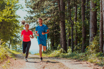 Couple enjoying in a healthy lifestyle while jogging on a country road through the beautiful sunny forest, exercise and fitness concept
