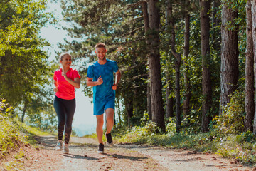 Fototapeta premium Couple enjoying in a healthy lifestyle while jogging on a country road through the beautiful sunny forest, exercise and fitness concept