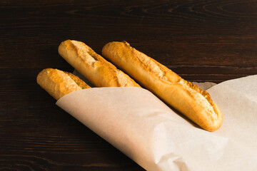 Delicious baguettes from the bakery wrapped in baking paper, on a dark wooden background