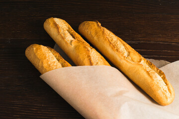 Delicious baguettes from the bakery wrapped in baking paper, on a dark wooden background