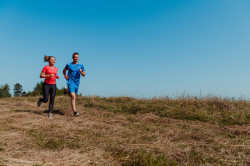Naklejka na ściany i meble Couple enjoying in a healthy lifestyle while jogging on a country road through the beautiful sunny forest, exercise and fitness concept