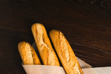 Delicious baguettes from the bakery close-up, wrapped in baking paper, on a dark wooden background with copy space