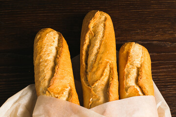 Delicious baguettes from the bakery wrapped in baking paper, on a dark wooden background