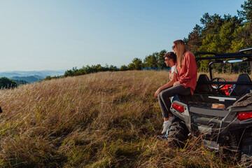 Naklejka na ściany i meble Young happy excited couple enjoying beautiful sunny day while driving a off road buggy car on mountain nature