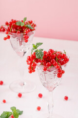 Fresh red currants in crystal glasses on a pink background