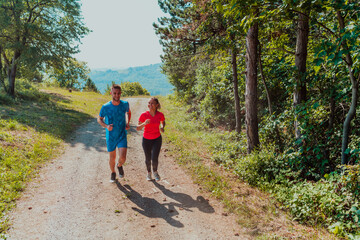 Obraz premium Couple enjoying in a healthy lifestyle while jogging on a country road through the beautiful sunny forest, exercise and fitness concept