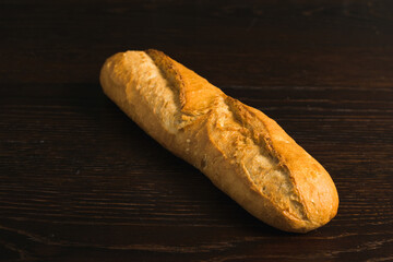 Appetizing french baguette with crust on dark wooden table, background with space for text