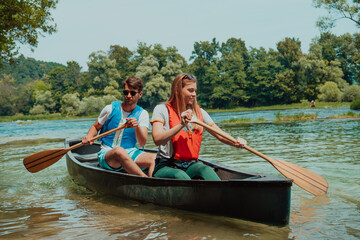 Couple adventurous explorer friends are canoeing in a wild river surrounded by the beautiful nature