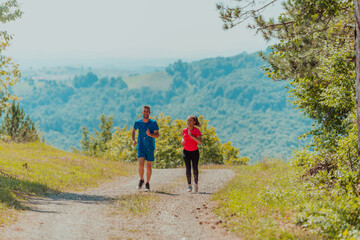 Obraz premium Couple enjoying in a healthy lifestyle while jogging on a country road through the beautiful sunny forest, exercise and fitness concept