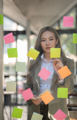 Asian businesswomen use post-it notes on glass walls to write strategy business plans to development grow to success