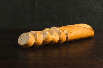 French baguette with appetizing crust cut into pieces on wooden table close-up, dark wooden background with copy space