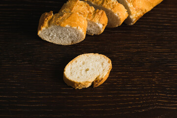 French baguette with appetizing crust cut into pieces on wooden table close-up, top view, dark wooden background with copy space