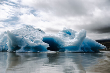 View of a blue iceberg broken off from the glacier tongue of Fjallsjökull in the glacier lagoon Fjallsárlón in Iceland on a cloudy day. With a view of Öræfajökull in the background.