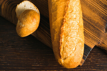 Fragrant, fresh French baguette with crust on a dark wooden cutting board, flatlay
