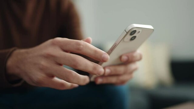 Young hispanic man using smartphone sitting on sofa at home