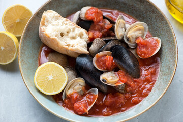 Plate with steamed mussels and littleneck clams in thick tomato broth, middle close-up, horizontal shot, selective focus