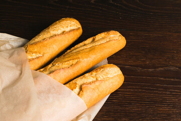 Delicious baguettes from the bakery close-up, wrapped in baking paper, on a dark wooden background with copy space
