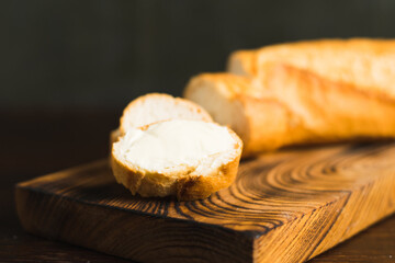 A slice of baguette with butter macro on a wooden background. Sliced French baguette on a wooden cutting board