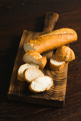 Slice of baguette with butter and sliced French baguette on wooden cutting board close-up, top view