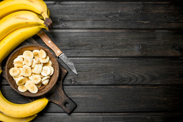 Bananas and banana pieces in a wooden plate on a cutting Board with a knife.