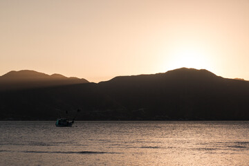 Naklejka premium Sol se pondo atrás das montanhas iluminando o mar