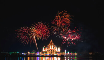 Beautiful fireworks in night sky over Wat Krok Krak Thai temple with decorative lighting and light reflection on river surface in annual festival area at night in Samutsakhon, Thailand - obrazy, fototapety, plakaty