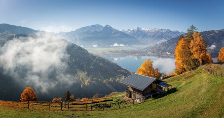 Naklejka premium Colorful foggy morning in the Alps mountains. autumn foggy scenery. Amazing nature background. Mountainous autumn landscape. Red folliage on trees and fog in the distant valley. Zell am see lake