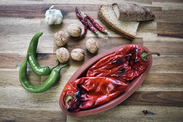 Roasted red peppers in a ceramic pot on a wooden table, accompanied by two slices of traditional natural wheat bread, red and green peppers, a head of garlic. Healthy eating food low carb diet