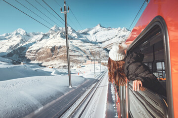 Happy woman traveler looks out from window traveling by train in beautiful winter mountains, Travel...
