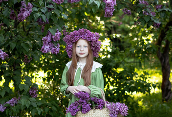 little girl with long red hair with a wreath of lilacs on her head in the garden in spring