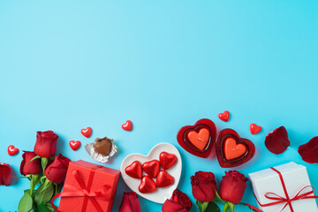 Valentines day celebration concept with heart shape chocolate, gift box and  rose flowers on blue background. Top view. Flat lay