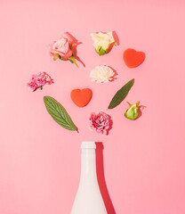 Champagne bottle with spring flowers and two hearts against pink background. Creative spring, summer and love idea.