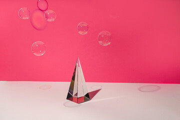 Glass pyramid prism and soap bubbles on pink background with colorful sunlight reflection horizontal